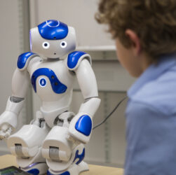 A boy watching a robot which is medium in size and have white with blue combo.