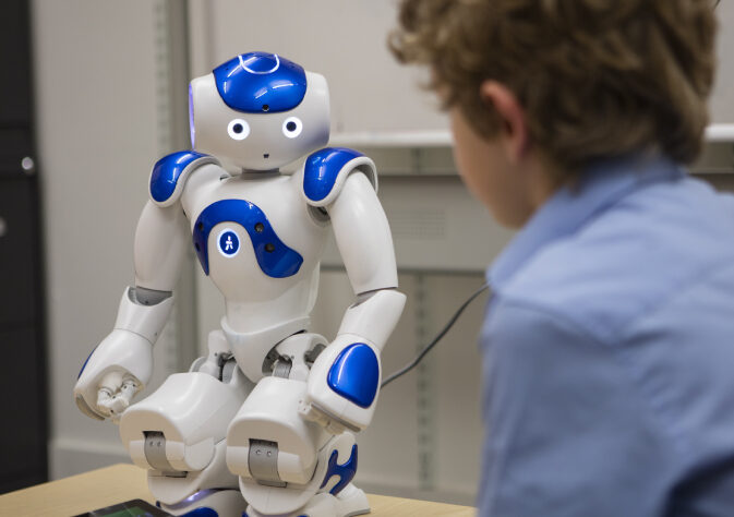 A boy watching a robot which is medium in size and have white with blue combo.