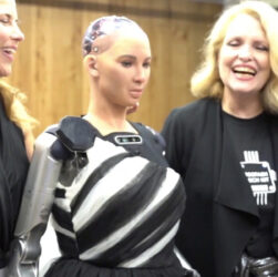 Two smiling women with a robot standing in between them