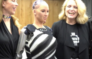Two smiling women with a robot standing in between them