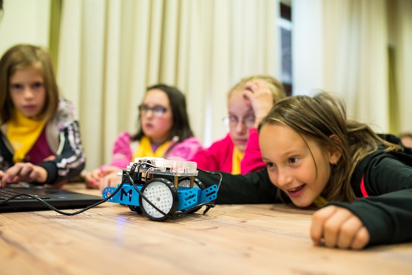 There are four little school kids experimenting with a mini robot which is connected to a laptop.
